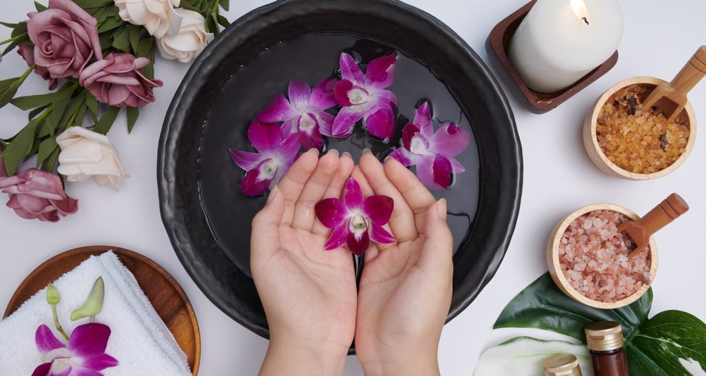 Hands soaking in water with flowers and therapy essentials