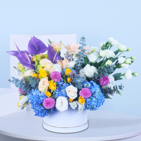 Elegant blue, white, and purple floral arrangement in a chic round box.
