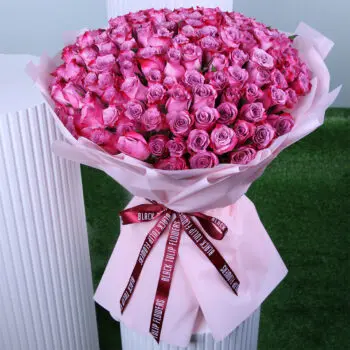 An elegant dark pink rose bouquet wrapped in a pink wrap and placed on a presentable table.