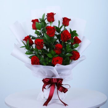 A bouquet of red roses hand-wrapped in a white sheet, placed on a presentable table.