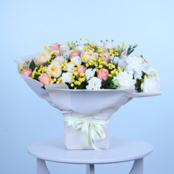 white and yellow flower arrangement with soft pastel tones, beautifully wrapped and placed on a white table.