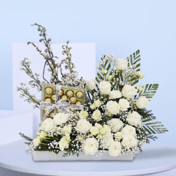 White roses with baby’s breath, Ferrero Rocher chocolates, and lush greens in a stylish floral gift arrangement.