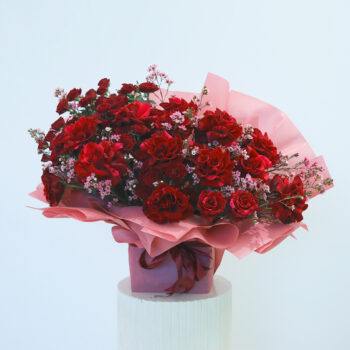 Red rose bouquet wrapped in pink displayed on a table.