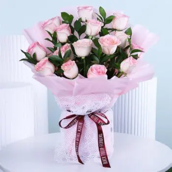 A bouquet of light pink roses wrapped in soft pink paper with a ribbon.