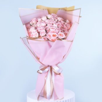 A bouquet of Pink flowers Warper in a pink and gold paper tied with a whote ribbon.