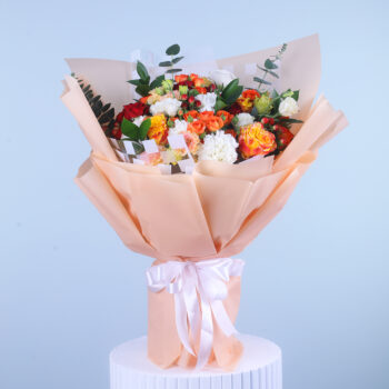 A colorful mixed flower bouquet wrapped in peach and ivory with a satin ribbon.