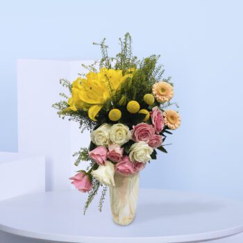 A marble vase filled with yellow lilies, pink and white roses, peach gerberas, and lush greenery.