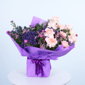 Bouquet of peach and purple flowers with violet wrapping placed on the top of a white round table.