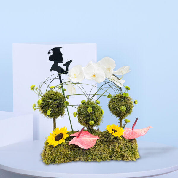 Graduation-themed flower arrangement with orchids, sunflowers, moss balls, anthuriums, and a graduate silhouette decoration.