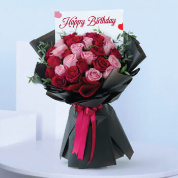 Birthday bouquet with pink and red roses wrapped in black paper and bright ribbon.