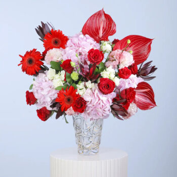 Pink hydrangeas, red anthuriums, red roses, red gerberas and white filler blooms in a clear glass vase arrangement
