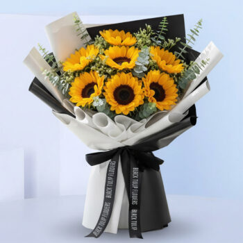 Bouquet featuring hand-tied sunflowers & eucalyptus in black-and-white wrap, finished with a ribbon bow.